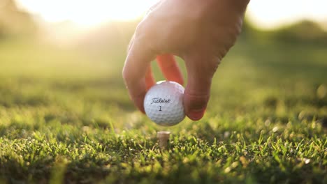 Titleist-Golf-Ball-Teed-Up-on-Grassy-Driving-Range---Close-up-of-Hand