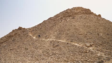 Hiker-climbing-trail-to-peak-of-Mount-Ramon-on-a-sunny-day-in-the-Negev-desert,-Israel
