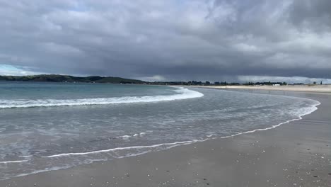 Low-wave-flowing-onto-beach-under-a-cloudy-grey-sky-in-Omaha-Warkworth-New-Zealand