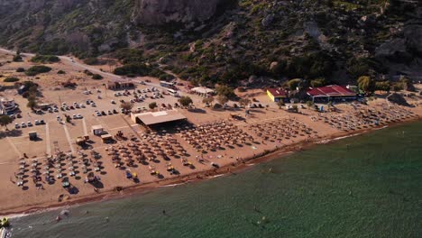 Aerial-View-Of-Broad-Unspoiled-Tsambika-Beach-With-Sun-Loungers-And-Umbrellas-On-Rhodes-Island-In-Greece