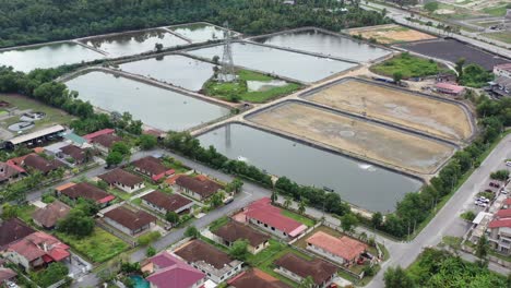 Drone-flyover-residential-neighborhood-in-manjung,-birds-eye-view-overlooking-at-surrounding-aquaculture-farming-controlled-facility-with-transmission-tower-in-the-middle,-malaysia,-southeast-Asia