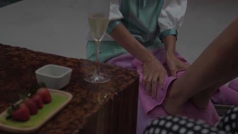 A-masseuse-doing-a-leg-massage,-strawberries-and-a-glass-of-champagne-on-a-wooden-table