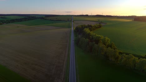 Aerial-Drone-Birds-Eye-View-Of-European-Countryside-Road-At-Sunset-With-Wind-Turbines-On-The-Horizon-In-Czech-Republic