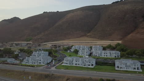 Drone-shot-slowly-flying-over-highway-with-large-house-and-condo-coastal-neighborhood-in-Pismo-Beach,-CA