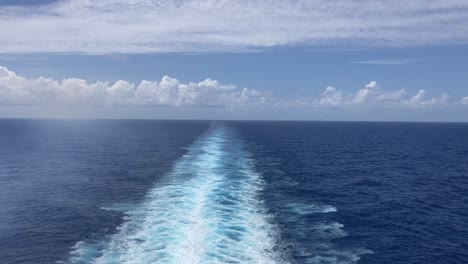Wake-behind-large-ship-on-the-ocean-with-sunny-blue-sky-and-clouds-on-horizon
