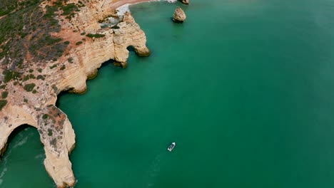 Pan-up-drone-footage-from-the-Algarve-Coast-as-a-motorboat-is-passing-by