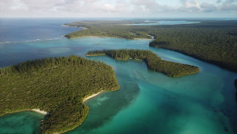 Slow-flyover-above-small,-forested-sunlit-islands-in-Oro-Bay,-Isle-of-Pines