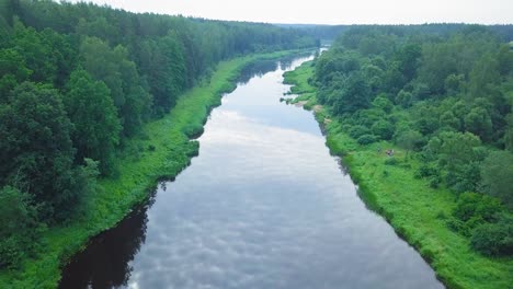Aerial-view-of-a-Venta-river-on-a-sunny-summer-day,-lush-green-trees-and-meadows,-beautiful-rural-landscape,-wide-angle-drone-shot-moving-forward