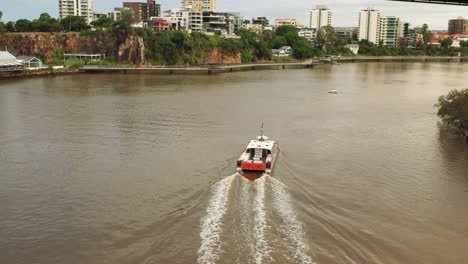 Following-a-ferry-flying-under-the-Story-Bridge-on-the-Brisbane-River,-brown-water-after-recent-flooding,drone-footage