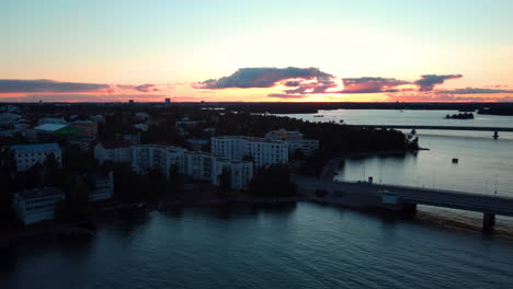 Aerial-view-of-the-Lauttasaarensilta-bridge-and-the-Lauttasaari-cityscape,-dusk-in-Helsinki,-Finland---tracking,-drone-shot