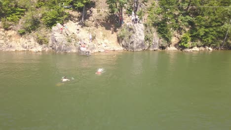 Vista-De-Drones-De-Personas-Jugando-Y-Nadando-En-Un-Lago-Cálido-Y-Bronceándose-En-La-Costa