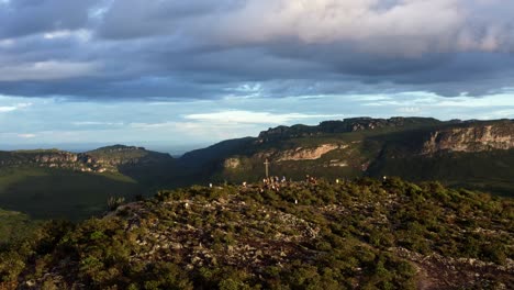 Dolly-Out-Flying-Drone-Landschaftsaufnahme-Der-Spitze-Des-Morro-Do-Pai-Inacio-Im-Nationalpark-Chapada-Diamantina-Im-Norden-Brasiliens-Mit-Wanderern,-Die-An-Einem-Warmen,-Sonnigen-Sommerabend-Ein-Riesiges-Kreuz-Umgeben