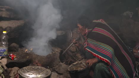 Native-Bolivian-Grandmother-Blows-Air-in-Traditional-Stove,-Prepares-for-Cooking