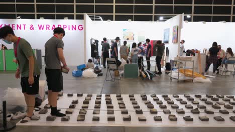 During-the-setup-and-installation-day,-art-exhibitors-prepare-ahead-of-the-opening-of-a-contemporary-art-fair-as-they-hand-paintings-on-the-wall-and-finish-up-with-the-decoration