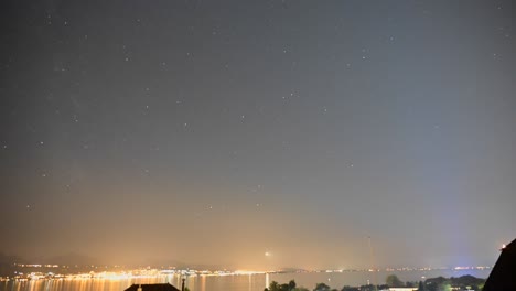 Starry-night-above-Lake-Geneva,-the-sky-is-moving-and-the-lights-of-the-cities-of-Evian-and-Lausanne-create-a-halo-of-light,-timelapse