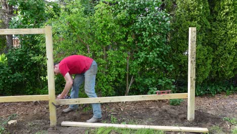 Man-uses-cordless-power-drill-to-screw-wooden-fence,-static-view