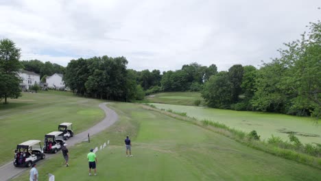 golfer-hits-tee-shot-over-swampy-pond,-aerial-drone-rise
