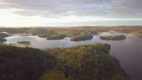 Weitwinkelaufnahme-Des-Sonnenaufgangs-Aus-Der-Luft,-Die-über-Die-Herbstwaldfarben-In-Richtung-Nebliger-Seen-Mit-Nebelbedeckten-Inseln-In-Kawarthas,-Ontario,-Kanada,-Fliegt