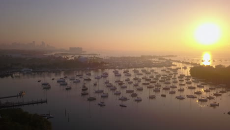 Aerial-high-angle-fly-past-boat-filled-harbor-and-sunrise