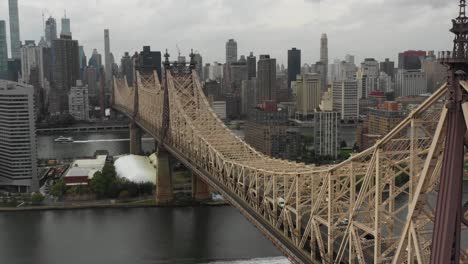 Long-side-sliding-drone-aerial-view-of-the-Queensboro-Bridge-looking-towards-Manhattan,-NYC-and-Queens-in-the-daytime-with-cars-leaving-Manhattan-on-the-the-bridge-and-boats