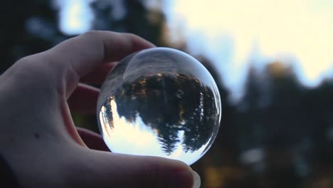 close-up-of-a-young-female-hand-holding-a-crystal-ball-reflecting-landscape-in-an-autumnal-forest-while-spinning-around