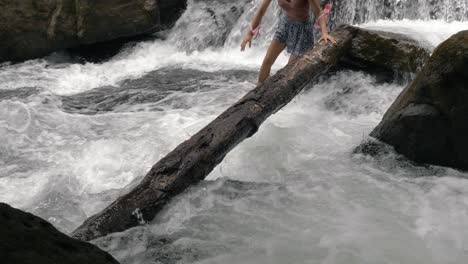 Caucasian-girl-walks-on-wooden-log-and-river-at-Klong-Chao-waterfall-and-enjoys,-Slow-motion