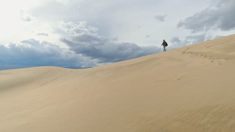 Slow-motion-of-a-lady-with-a-backpack-walking-along-the-ridge-of-a-high,-distant-sand-dune