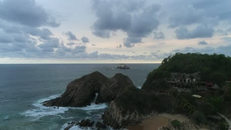 Aerial-jib-up-shot-from-Zipolite-beach-with-a-big-rock-formation,-Oaxaca