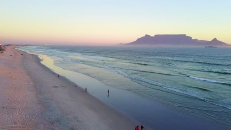 Luftaufnahme-Des-Sonnenuntergangs-Am-Strand-Von-Kapstadt-Mit-Dem-Tafelberg-Im-Hintergrund