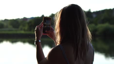 Backside-shot-of-a-girl-taking-photo-of-summer-lake-landscape