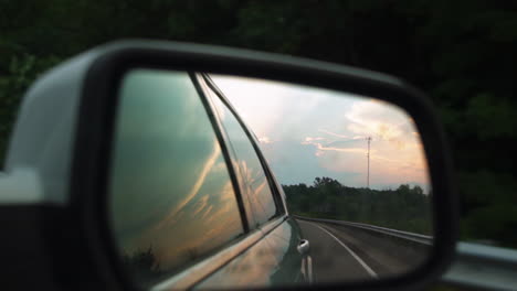 Golden-hour-cotton-candy-sky-in-side-view-mirror-of-driving-car-in-slow-motion