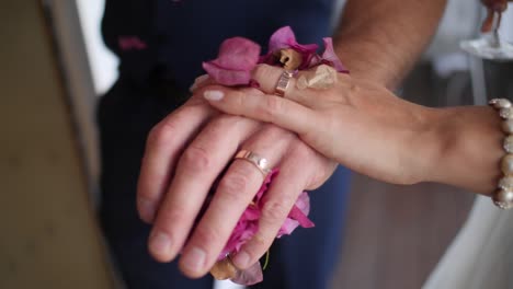 Zeitlupen-Nahaufnahme-Von-Braut-Und-Bräutigam,-Die-Sich-Mit-Hochzeitsringen-Und-Fallenden-Blütenblättern-An-Den-Händen-Halten