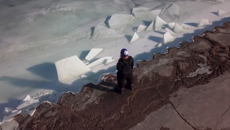 A-woman-in-a-blue-hat-holds-a-drink-while-standing-at-the-edge-of-a-frozen,-icy-lake-in-Canada