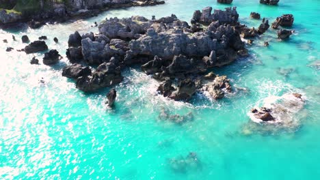 Aerial-view-of-sharp-pointy-rocks-in-turquoise-water-by-tropical-island