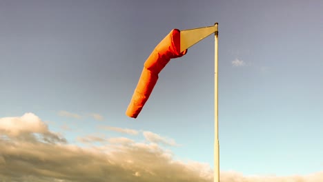 Ein-Orangefarbener-Windsack-Weht-Sanft-Im-Wind-Unter-Einem-Blauen-Himmel,-Während-Aus-Der-Ferne-Dunkle-Wolken-Aufziehen