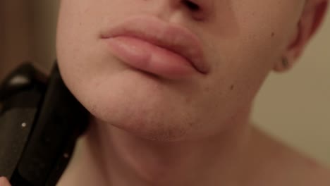 Close-up-shot-of-a-young-person-using-an-electric-trimmer-on-the-side-of-their-face-and-chin