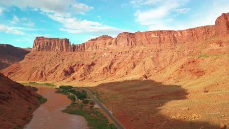 Aerial-descending-flight-over-a-scenic-road-along-the-Colorado-River-with-towering-canyon-walls-above