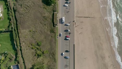Top-down-aerial-over-a-clifftop-luxury-house-and-a-beachside-road-with-parked-cars-and-traffic-moving-both-ways