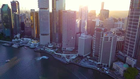 Aerial-view-of-a-modern-city-with-tall-buildings-and-public-ferry-by-the-river-at-sunset