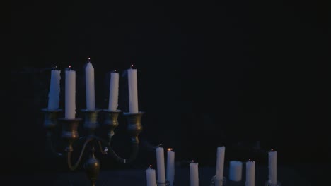 A-group-of-white-candles-some-on-a-candelabra-lit-up-then-blown-out-by-the-wind