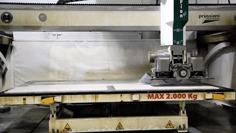 A-cutting-bench-at-a-countertop-factory,-with-an-automated-machine-saw-cutting-the-ending-part-of-a-granite-block-while-releasing-a-flow-of-cooling-water