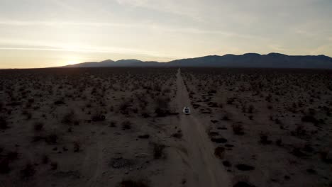 Aerial-Tracking-Shot-of-white-car-driving-on-trail-through-Mojave-Desert-plain