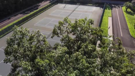 4K-Drohnenaufnahme-Eines-Tennisplatzes,-Der-Durch-Bäume-Hindurch-Erscheint