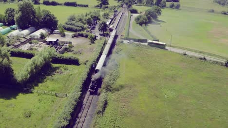 Wide-aerial-view-of-a-steam-train-leaving-Bodiam-station,-East-Sussex,-England