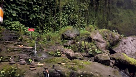 Schwenkansicht-Des-Ubud-Wasserfalls-Und-Der-üppig-Grünen-Dschungelmauer-Mit-Religiösem-Schrein-Zu-Ehren-Balinesischer-Götter