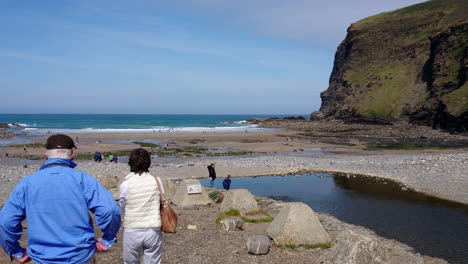 A-couple-of-senior-tourists-stop-at-Crackington-Haven-beach-in-Cornwall,-United-Kingdom,-where-walkers-swimmers-and-bathers-are-having-fun