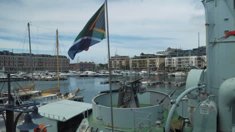 View-over-marina-at-V-A-Waterfront-in-Cape-Town,-South-African-flag-flapping-in-foreground
