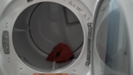 Close-up-of-a-man-loading-clothes-into-a-dryer-from-the-washing-machine-next-to-it-