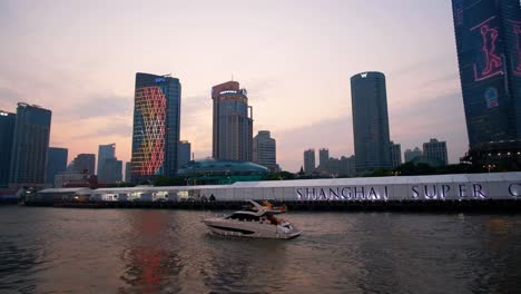 Sightseeing-boat-takes-tourists-on-an-evening-tour-of-Shanghai"s-famed-Huangpu-River-showcasing-spectacular-lights-on-nearby-commercial-buildings