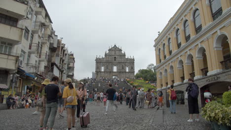 Numerous-tourists-walking-and-taking-pictures-on-a-hot-gray-cloudy-day-on-a-square-and-stairs-near-faÃ§ade-wall-of-Ruins-of-St